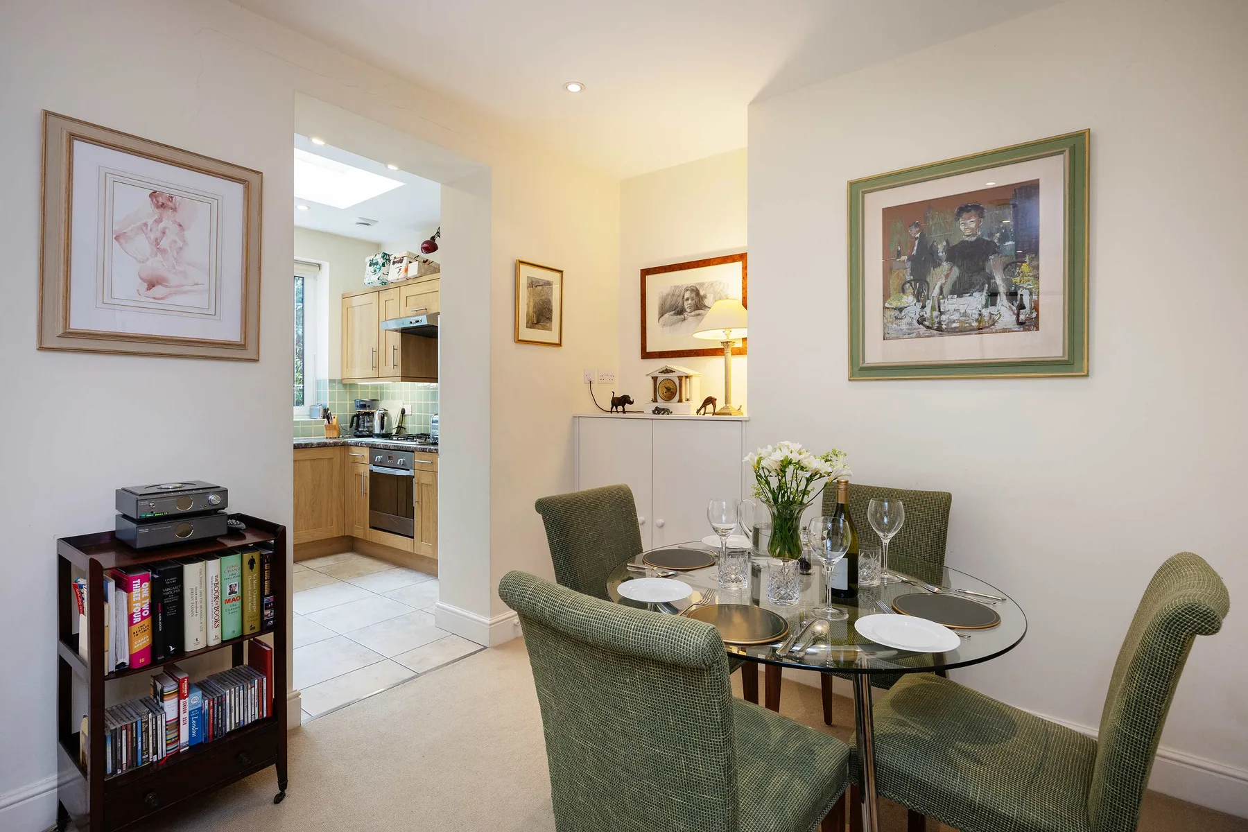 A dining area with a glass table and green upholstered seating beside an open kitchen.