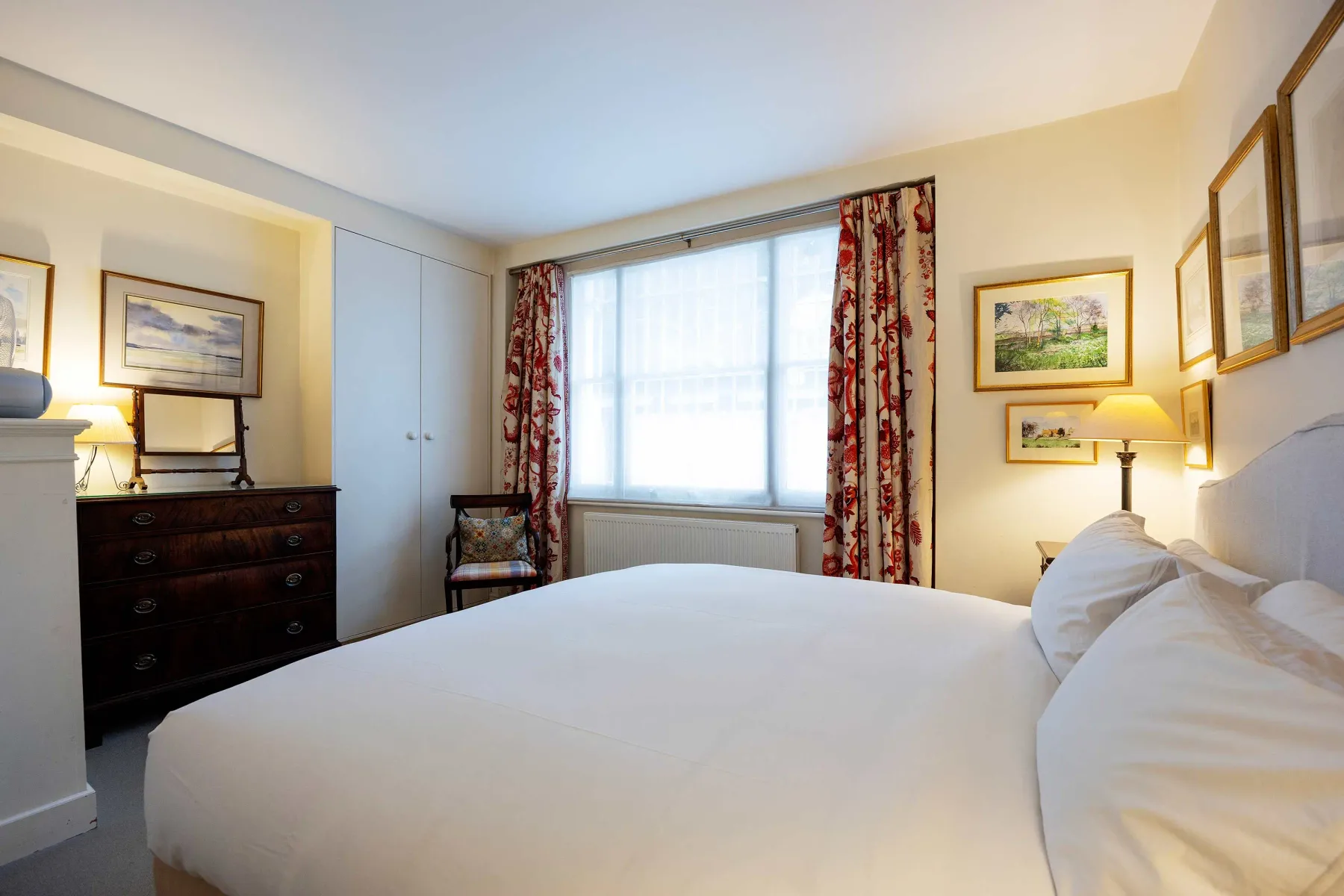 A bedroom with a large bed, curtained window, and framed pictures.