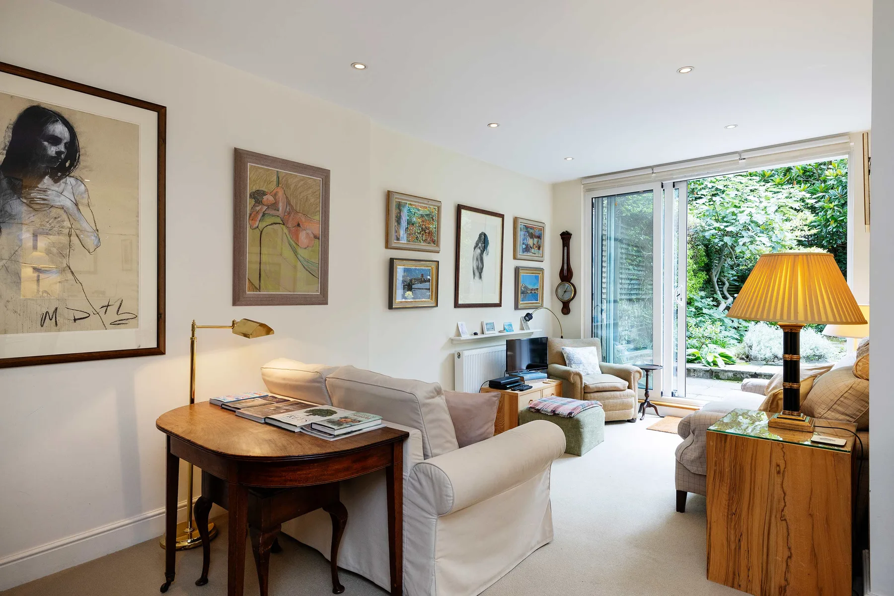 A bright living room with seating, framed artwork, and large windows overlooking greenery.