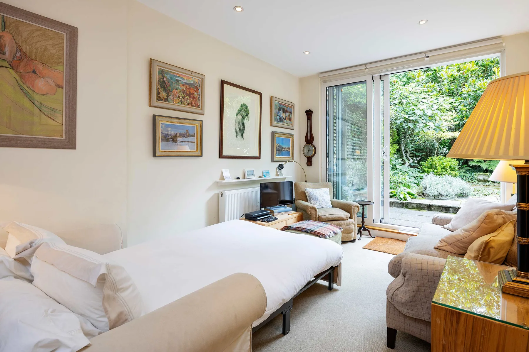 A bright bedroom with a bed, seating, and glass doors opening onto a garden.
