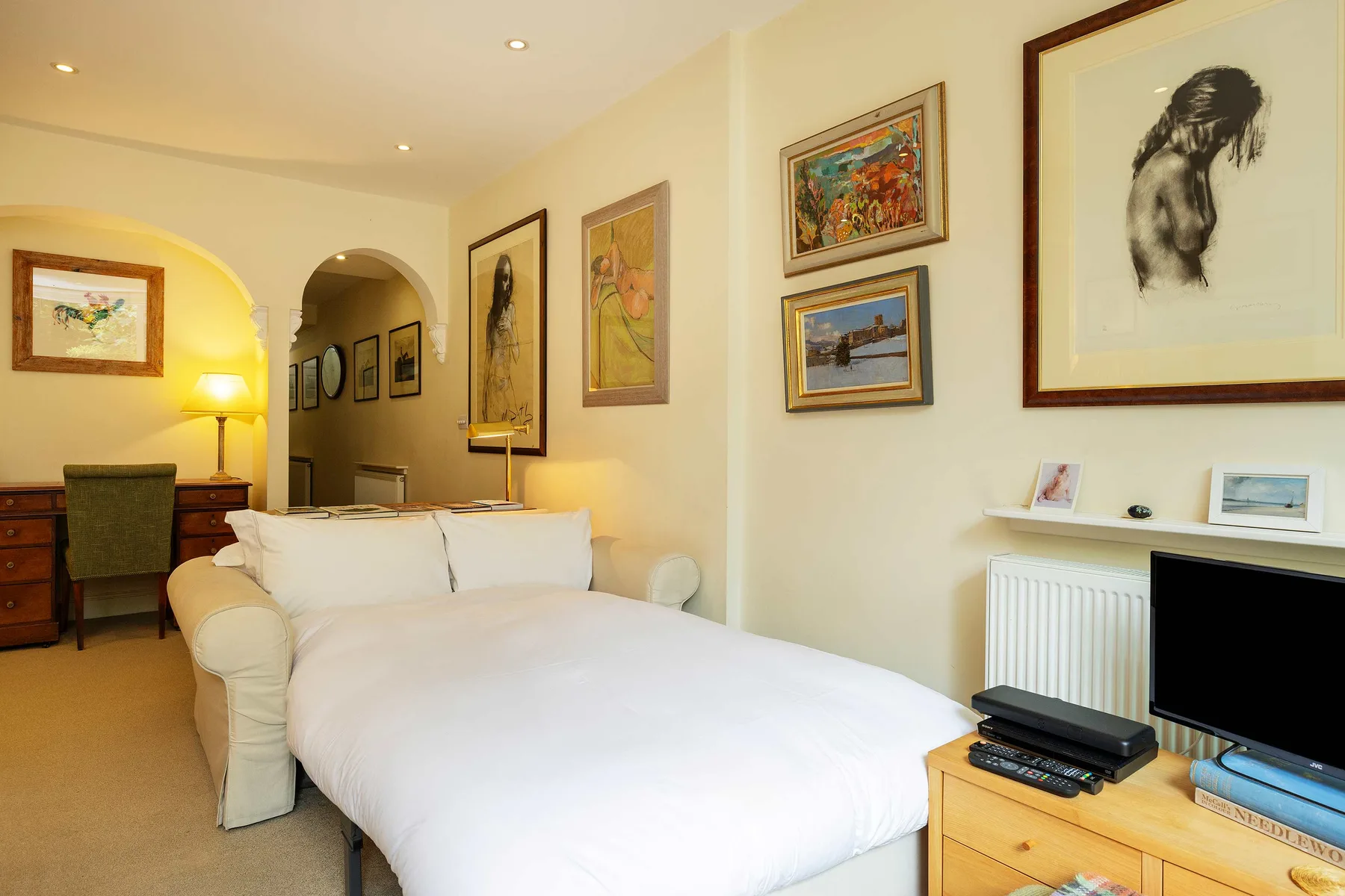 A bedroom with a white bed, framed artwork, and a television.