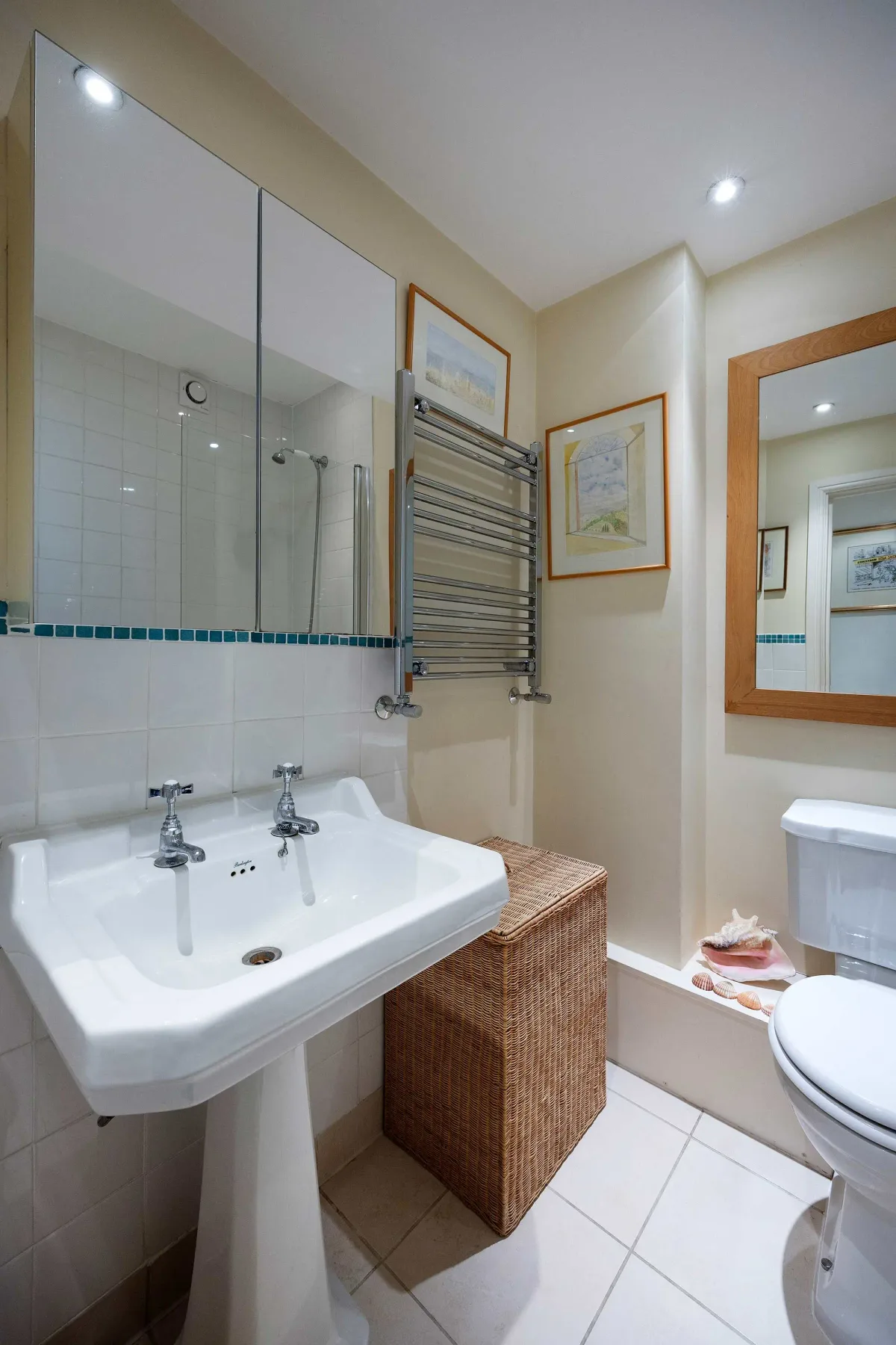 A tiled bathroom with a pedestal sink, wall mirror, and towel warmer.
