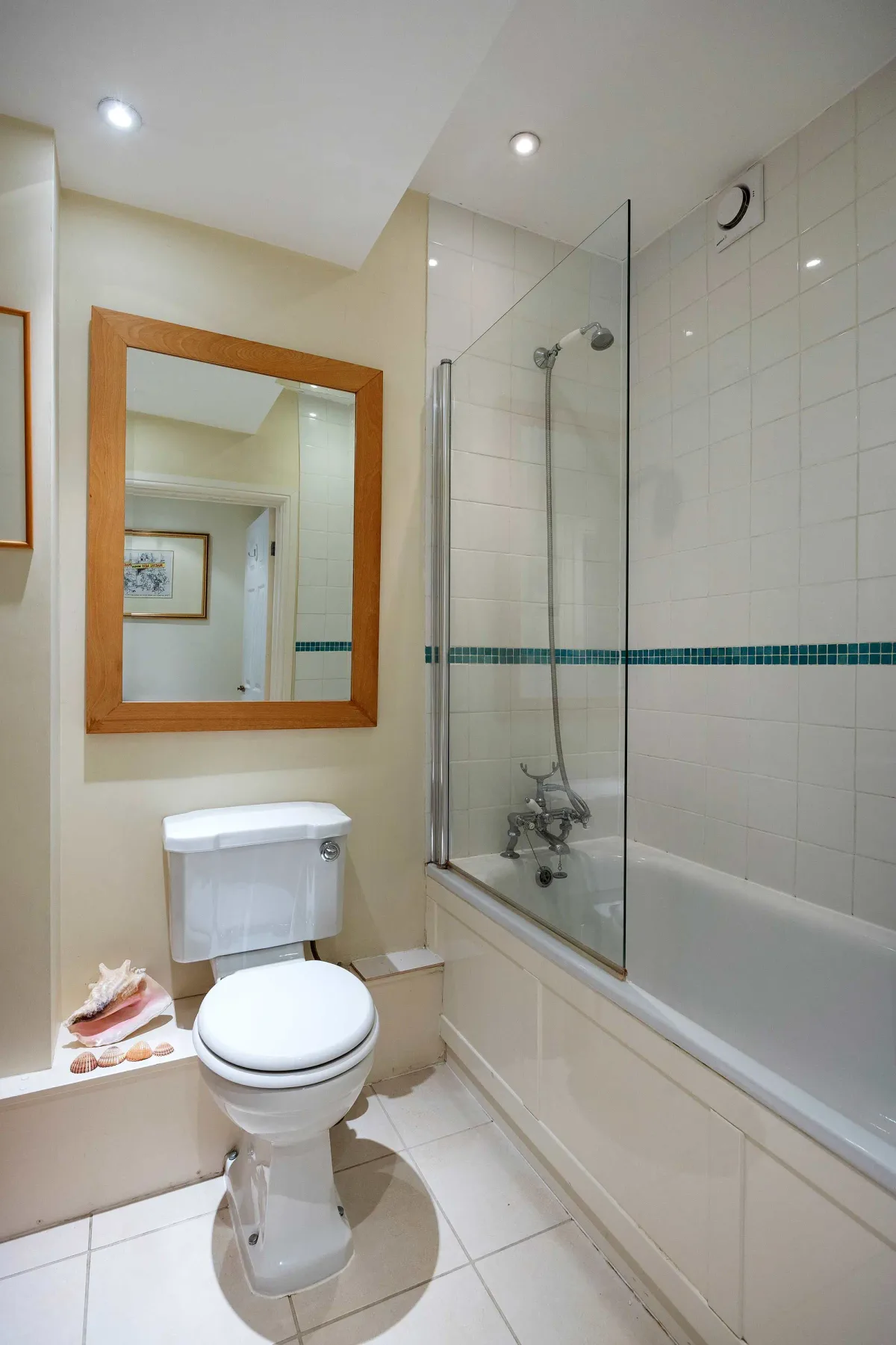 A tiled bathroom with a toilet, bathtub, and wall mirror.