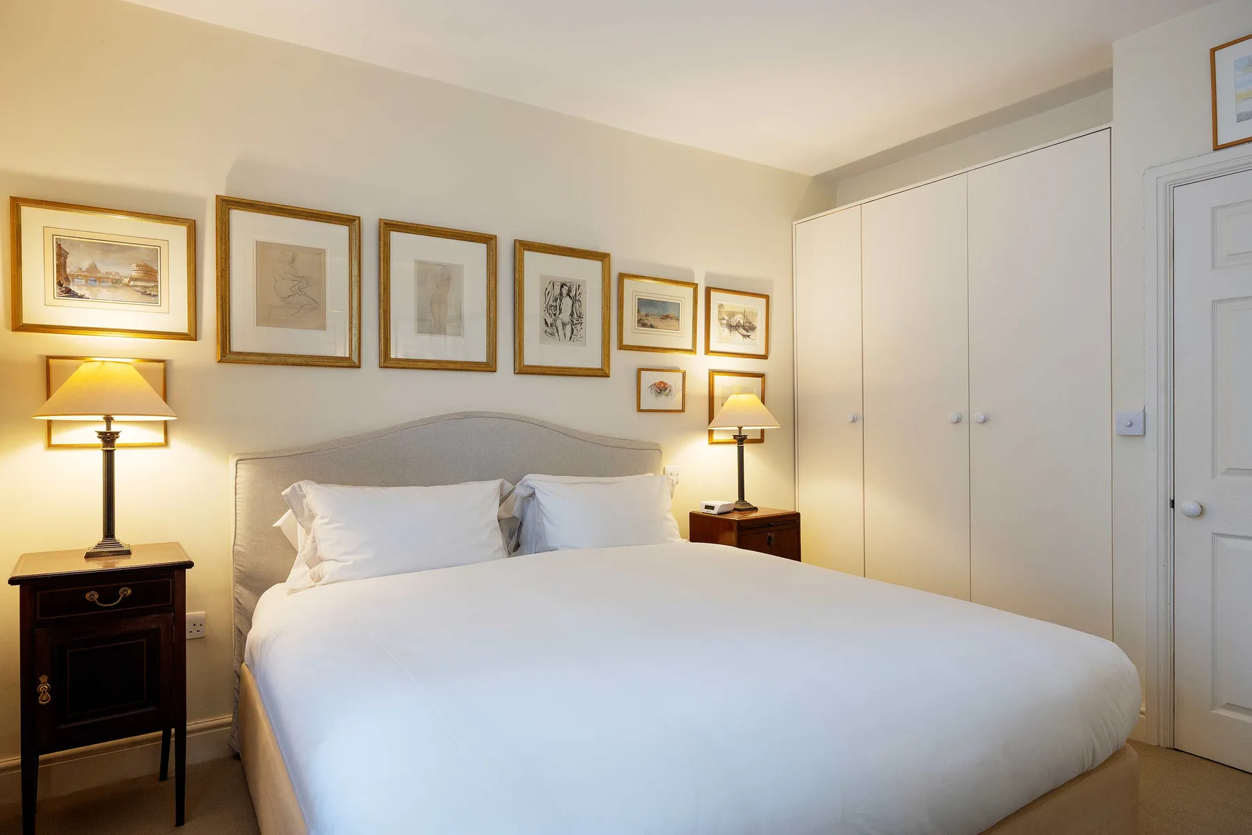 A bedroom with a neatly made bed, framed artwork, and bedside lamps.