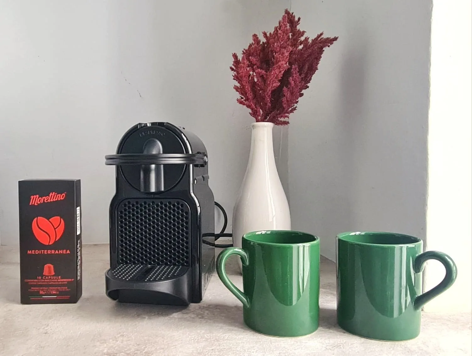 A countertop coffee setup with a black coffee machine and two green mugs.