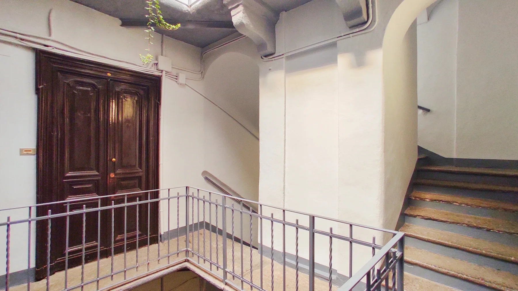An indoor stairwell with a dark wooden door and metal railings.