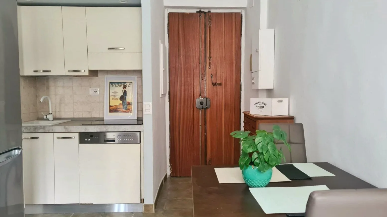A compact kitchen opens onto a dining area with a table and potted plant.