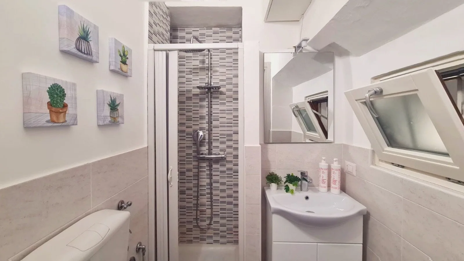 A compact bathroom with a tiled shower, sink, and wall art.