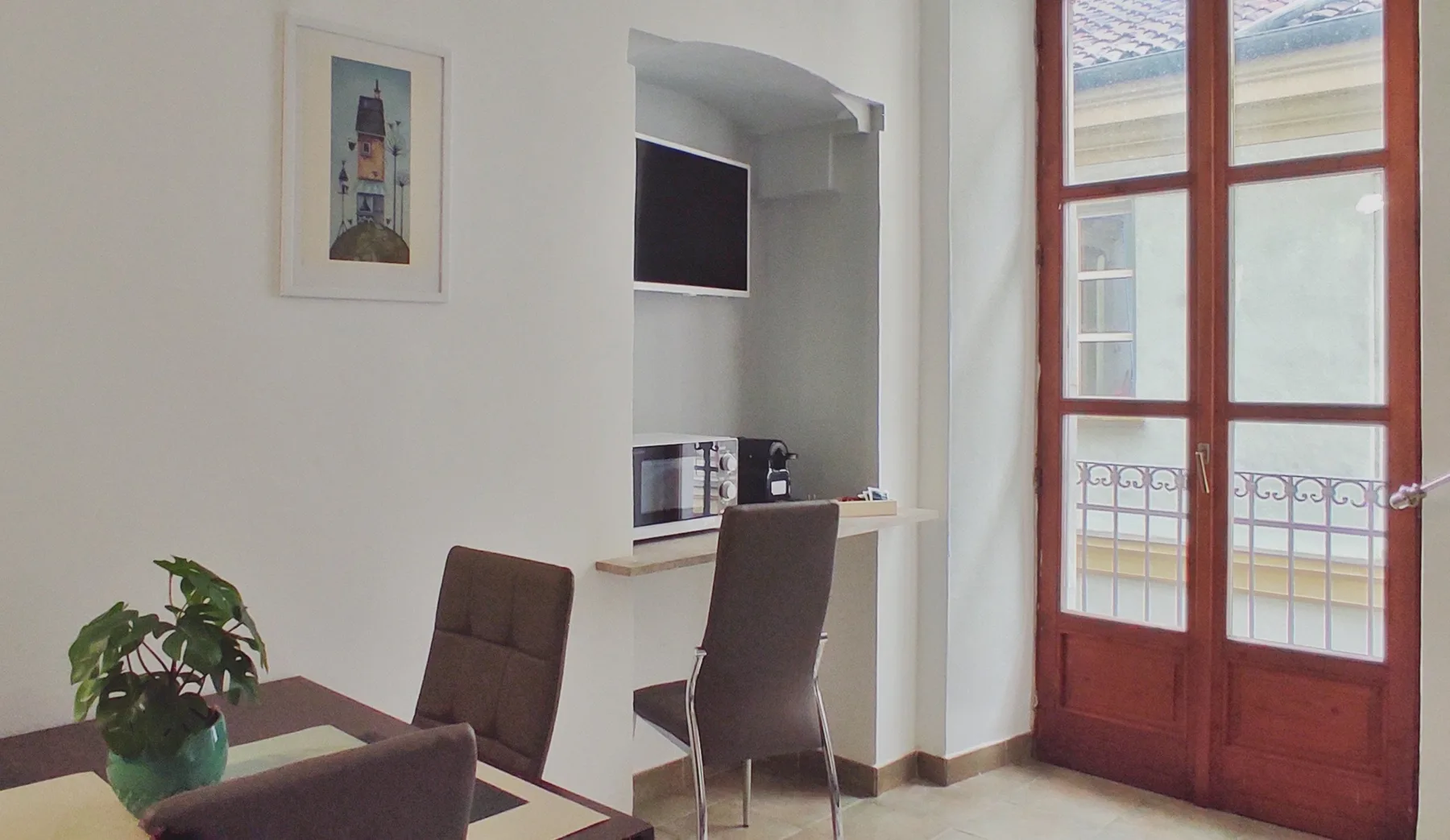 A dining area with a table, seating, and a work counter beside tall windows.