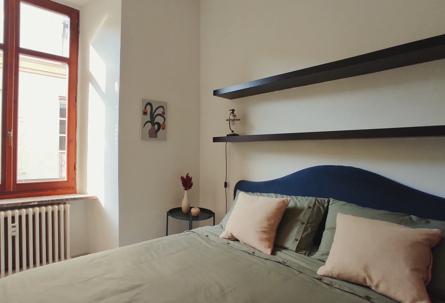 A bedroom with a bed, wall shelves, and a sunlit window.