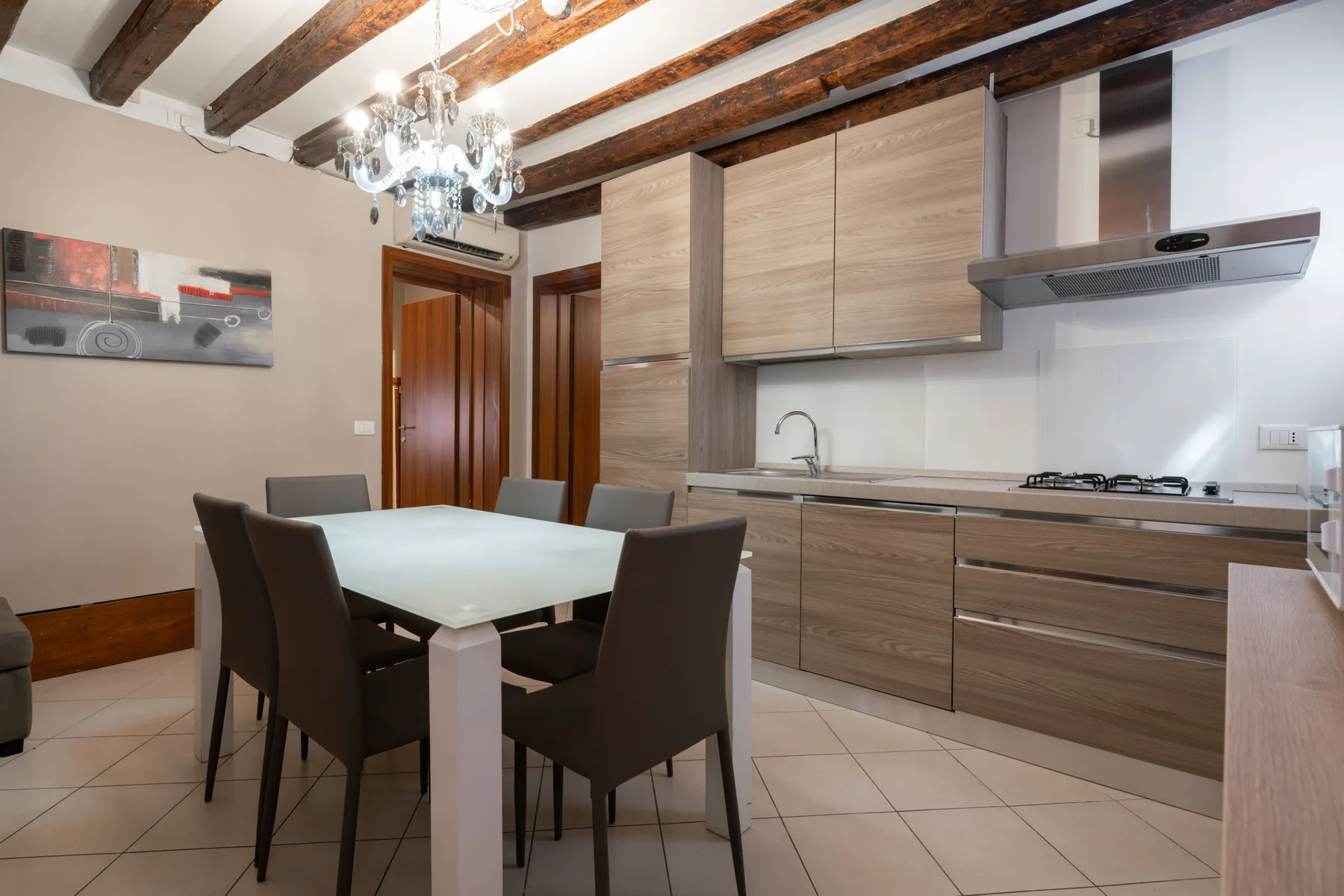 Un comedor y una cocina moderna se encuentran bajo vigas de techo expuestas.