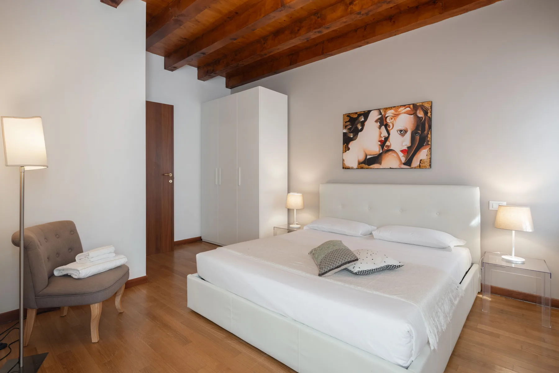 Un dormitorio con una cama grande, lámparas de noche y vigas de madera a la vista.
