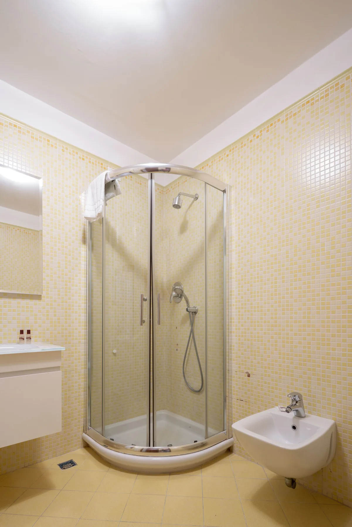 Un baño alicatado con una ducha curva de vidrio y un lavabo suspendido.