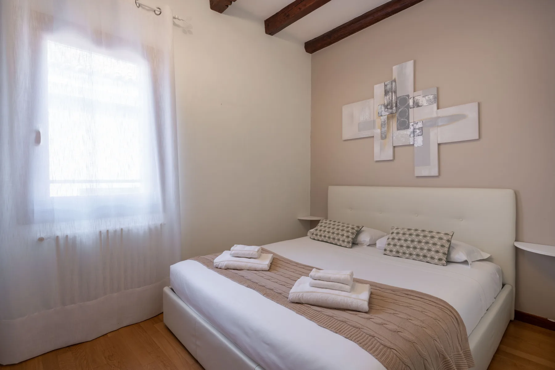 Un dormitorio con una cama bien arreglada bajo un cuadro abstracto.