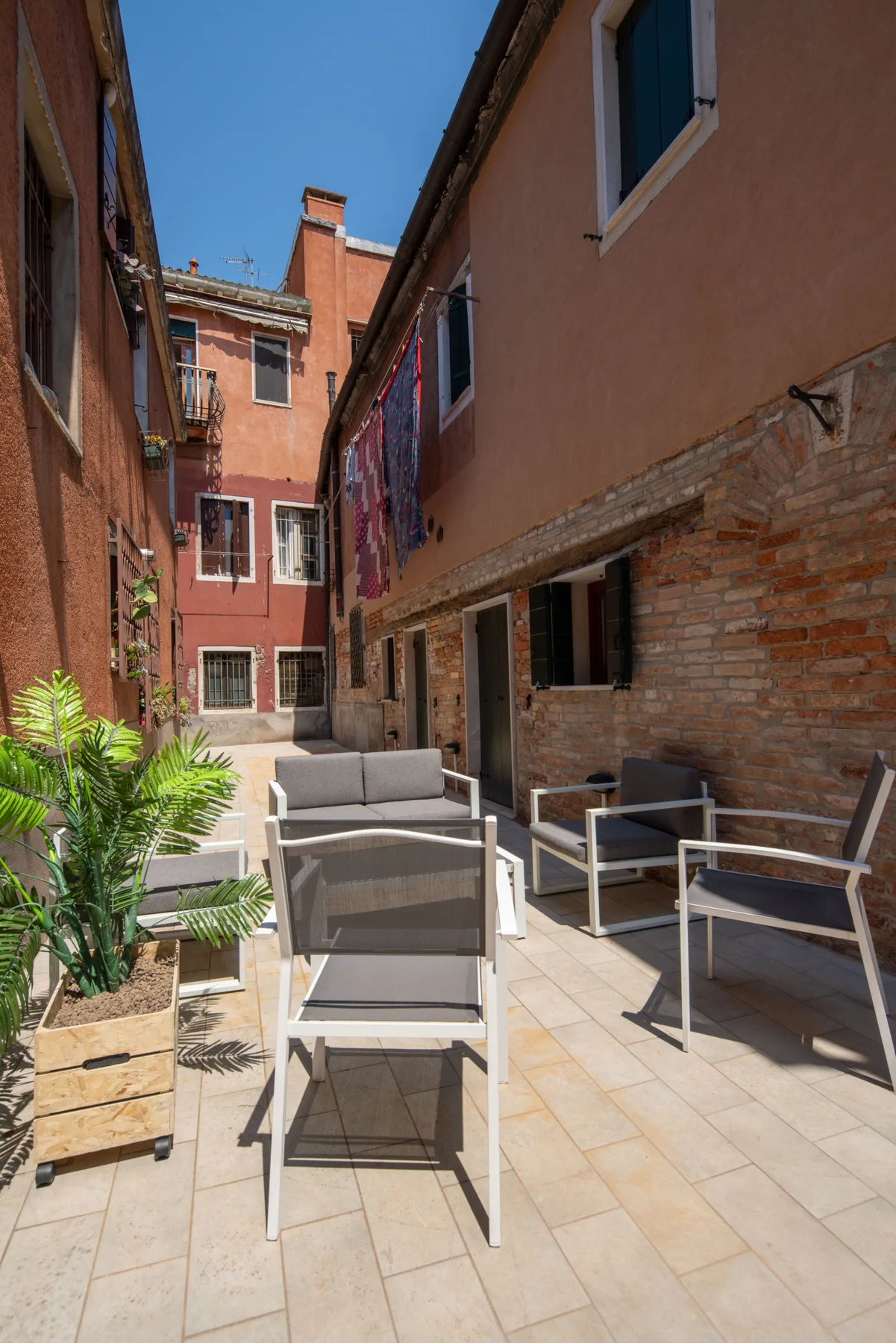 Un patio pavimentado entre edificios con asientos al aire libre y plantas en macetas.