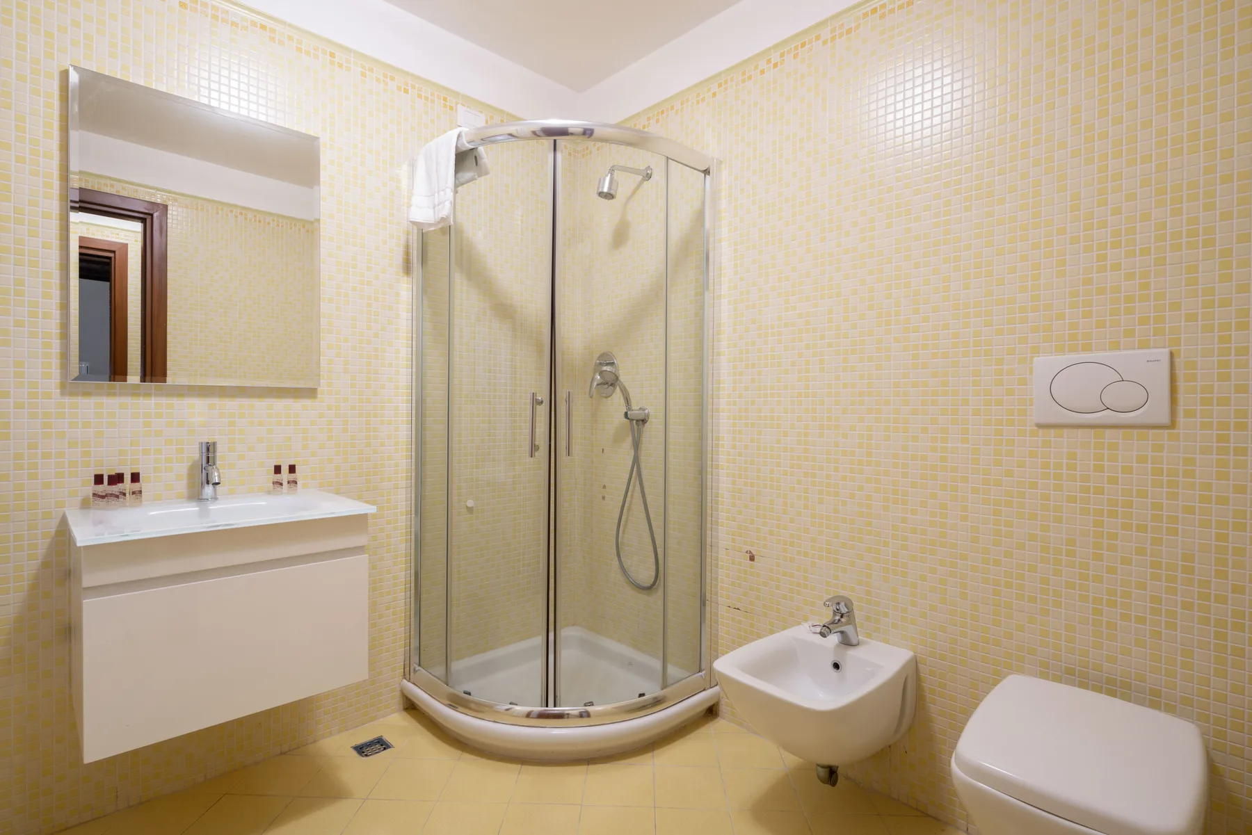 Un baño alicatado con ducha de vidrio, lavabo suspendido e inodoro.