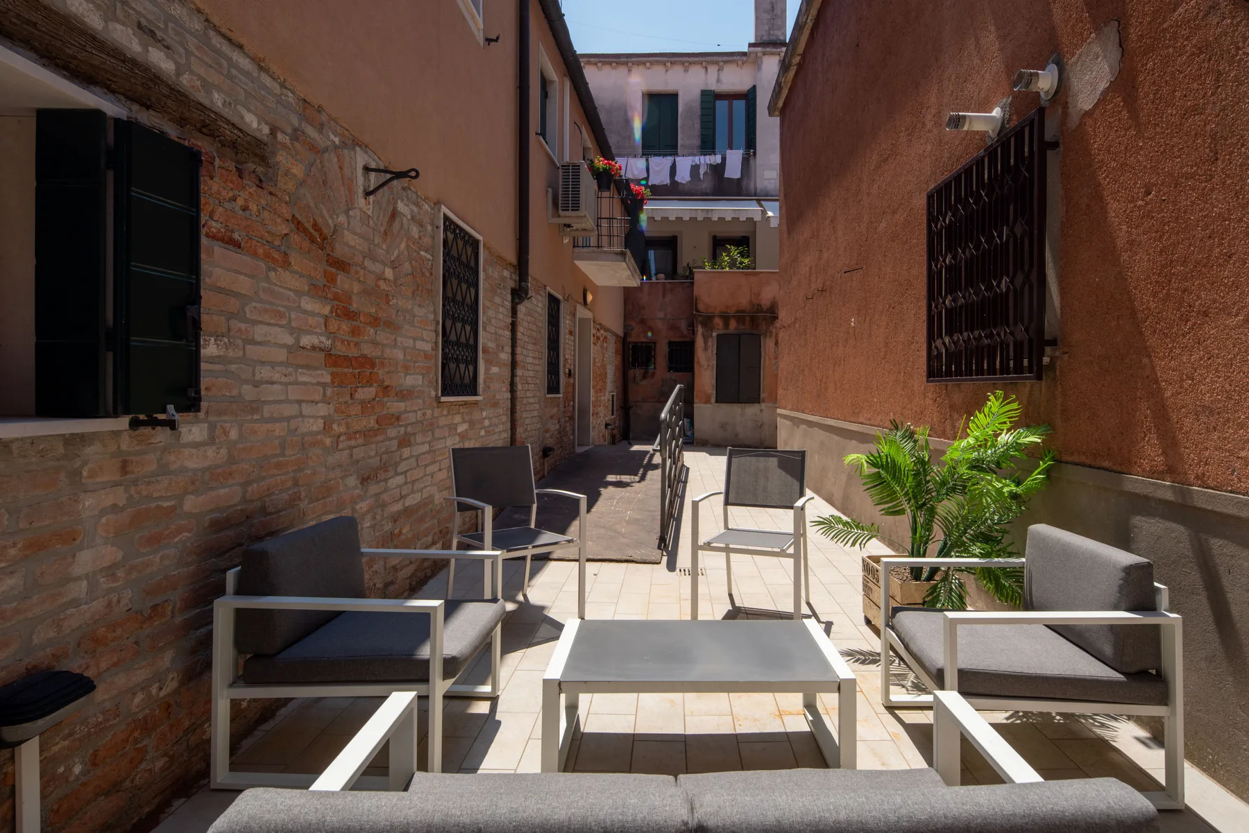 Un patio soleado con asientos al aire libre junto a un estrecho pasillo pavimentado.