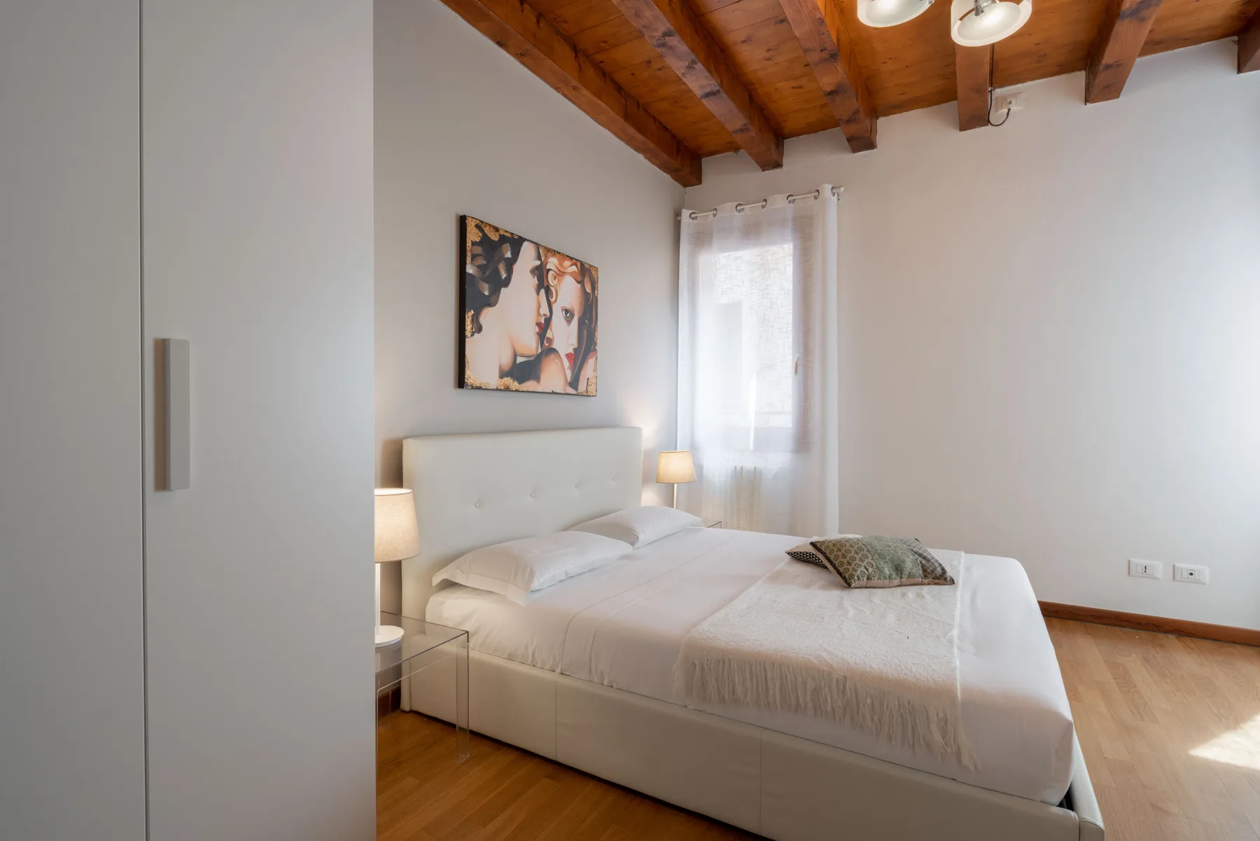 Un dormitorio con una cama bien tendida bajo vigas de madera expuestas.