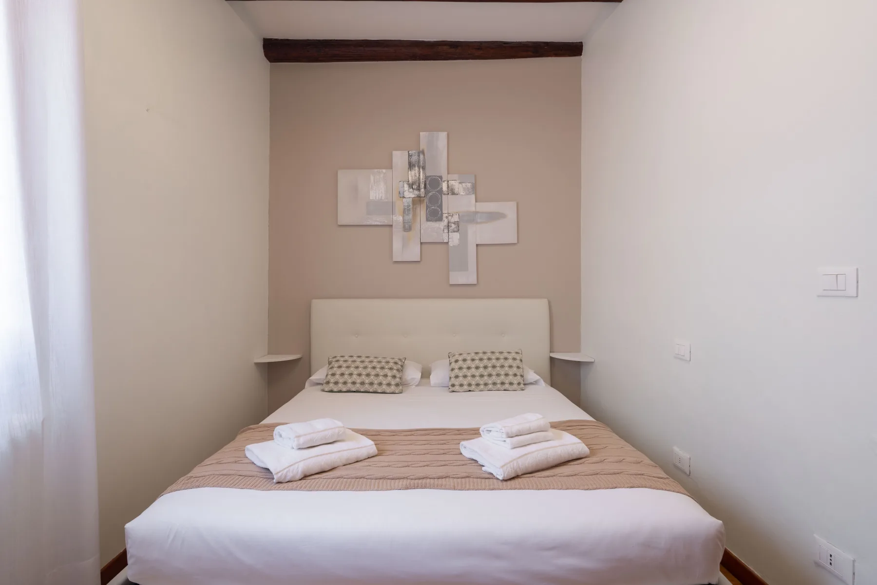 Un dormitorio con una cama bien tendida y arte abstracto sobre el cabecero.