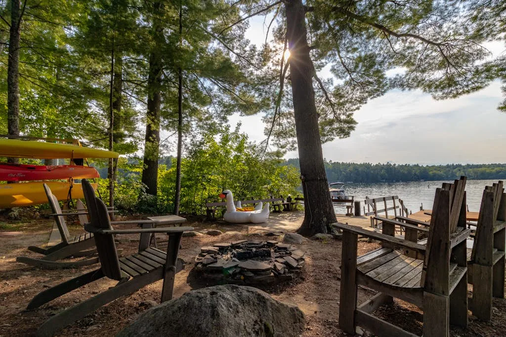 Zona de descanso junto al lago, a la sombra de árboles, con kayaks y un pequeño fogón.