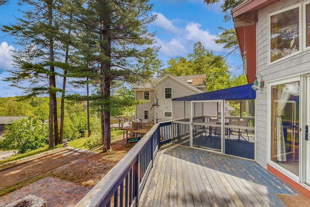 An outdoor deck overlooks a wooded yard, with a covered seating area beside the house.