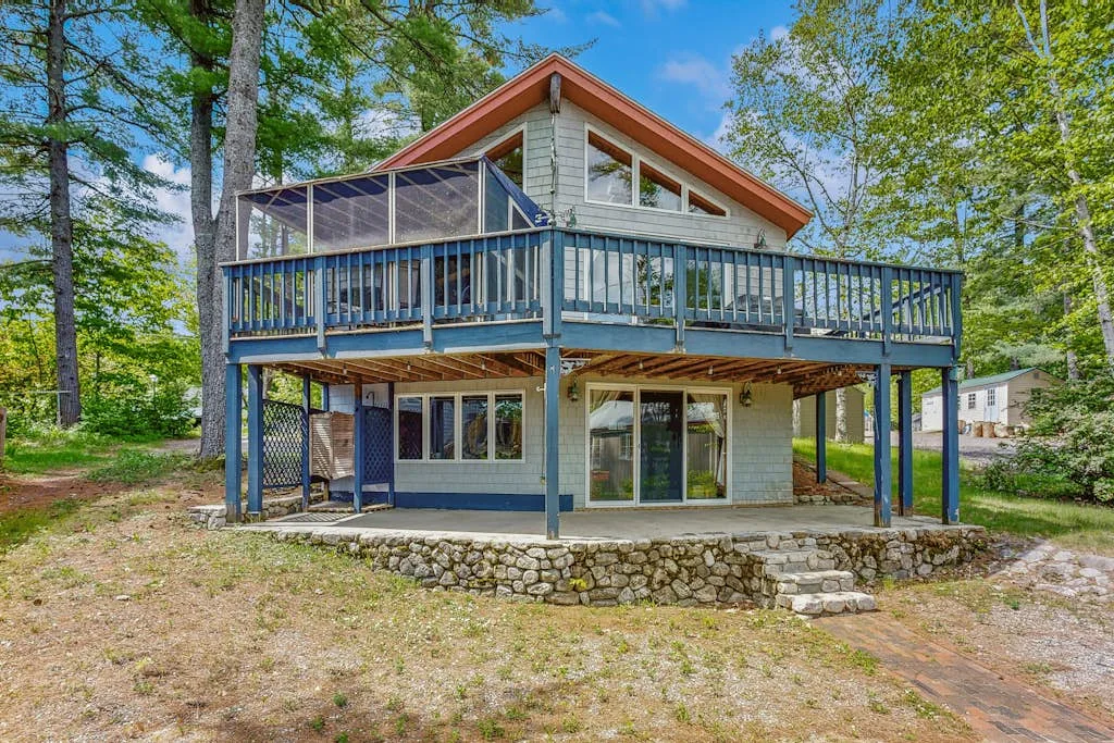 A two-story house with a broad raised deck stands among trees.