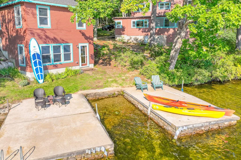 Un patio junto al lago con sillas, kayaks y edificios coloridos entre árboles.