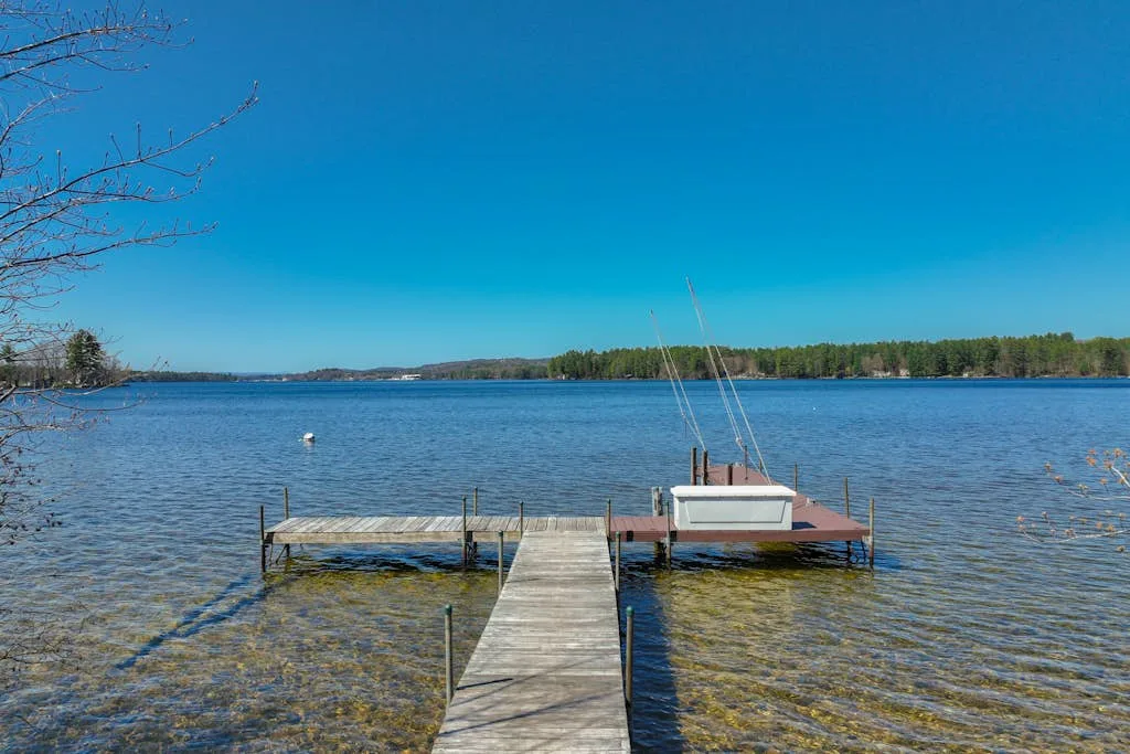 Un muelle de madera se adentra en un lago claro bajo un cielo azul.