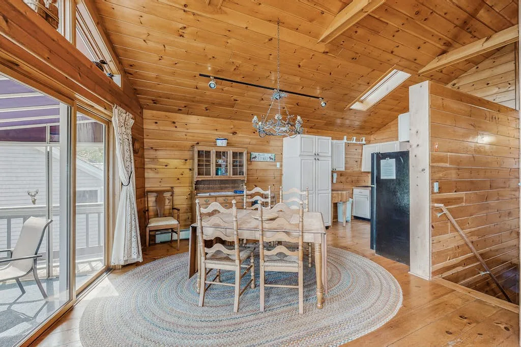 A wood-paneled dining area with a table, chairs, and a large round rug.