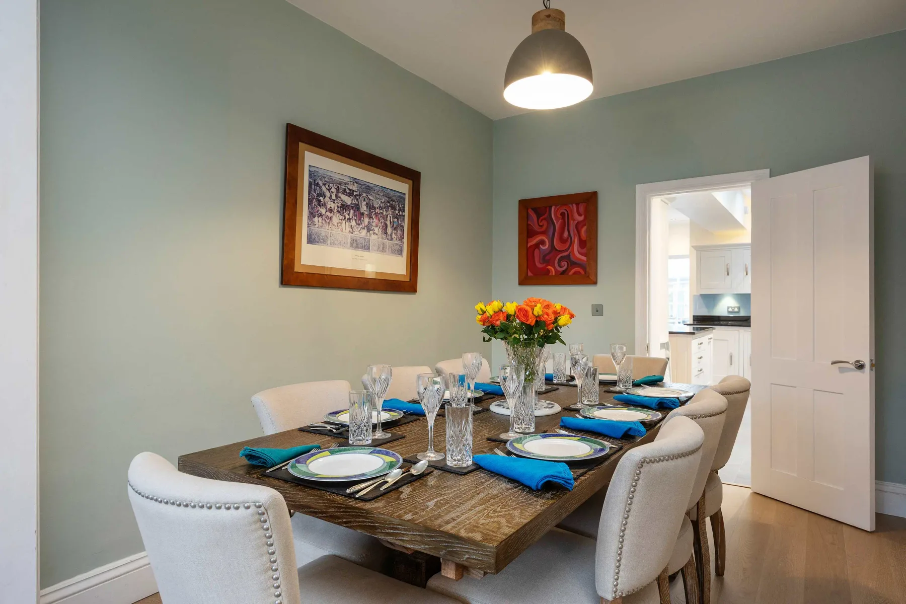 Un comedor con la mesa puesta y una obra enmarcada en la pared.