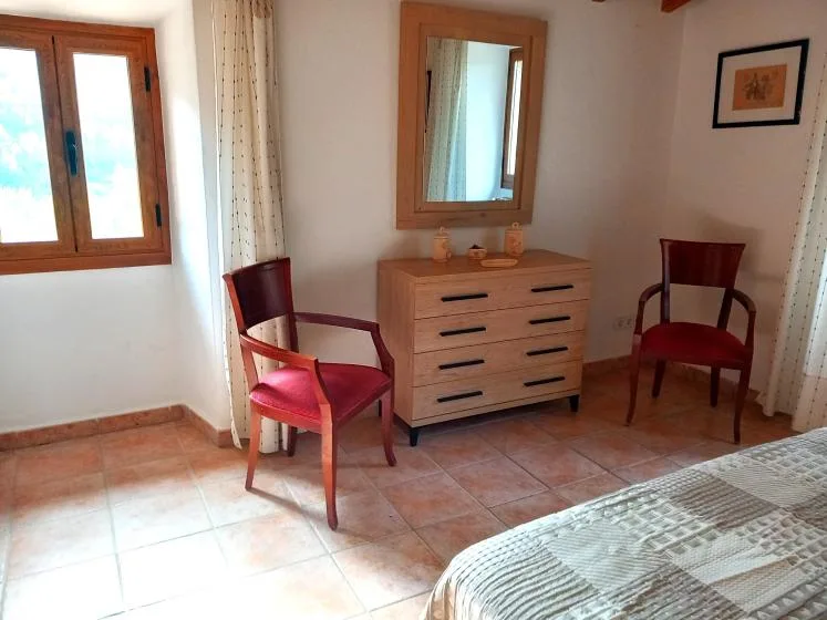A bedroom with a wooden dresser and mirror between two chairs.