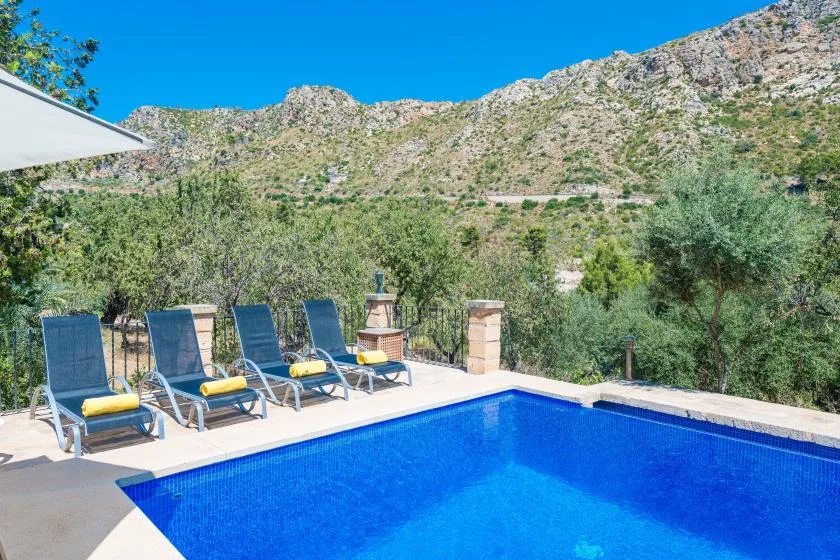 An outdoor swimming pool and lounge chairs overlook a green mountain landscape.