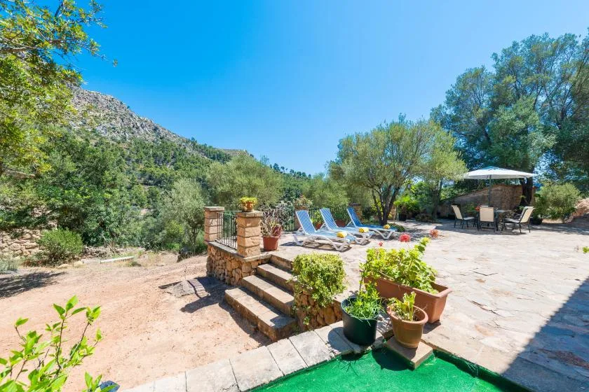 A sunny outdoor patio with lounge seating, potted plants, and a mountain view.