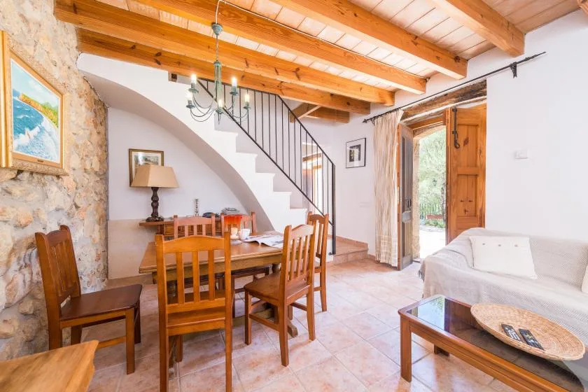 A dining and living area with wooden seating, exposed beams, and a staircase.