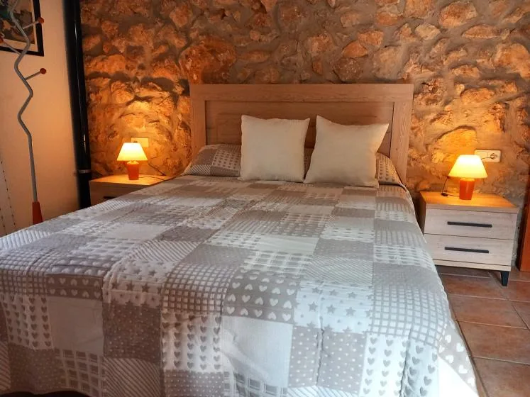 A bedroom with a bed dressed in a gray patchwork quilt.