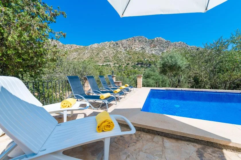 An outdoor swimming pool beside lounge seating, with a rocky hillside in the background.