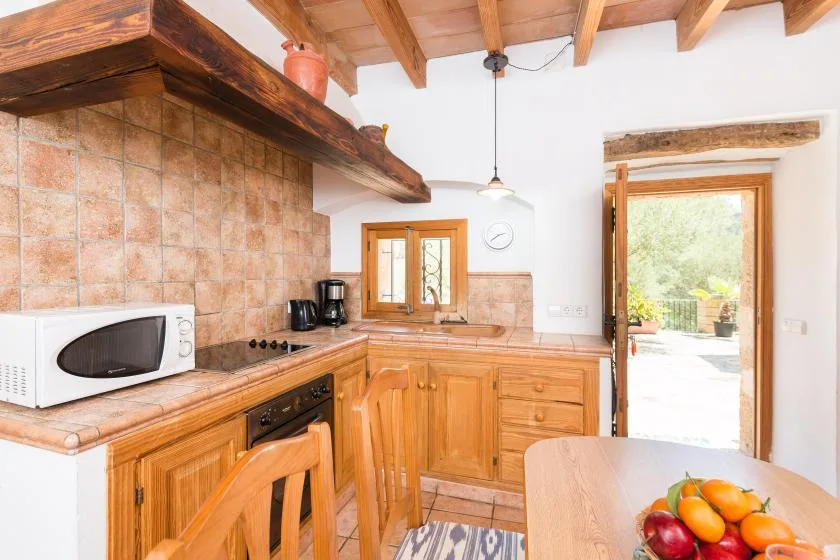 A rustic kitchen with wooden cabinets, a tiled backsplash, and a table with fruit.