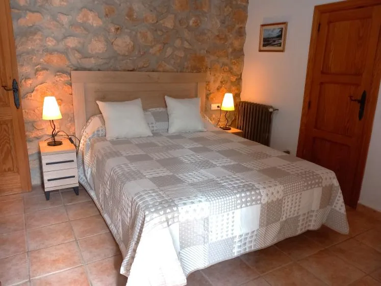 A bedroom with a double bed and bedside lamps against a stone wall.
