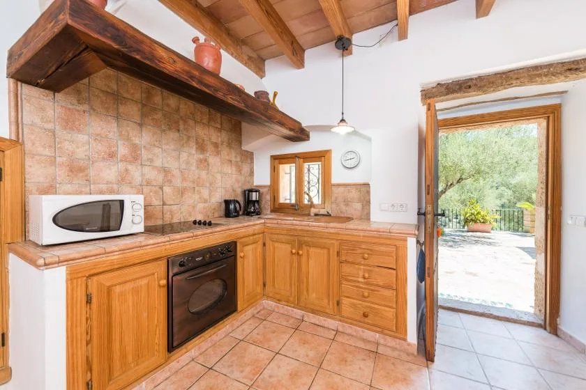 A rustic kitchen with wooden cabinets, tiled counters, and a doorway opening onto a patio.