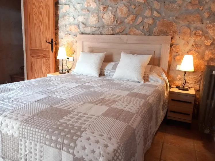 A bedroom with a large bed set against an exposed stone wall.