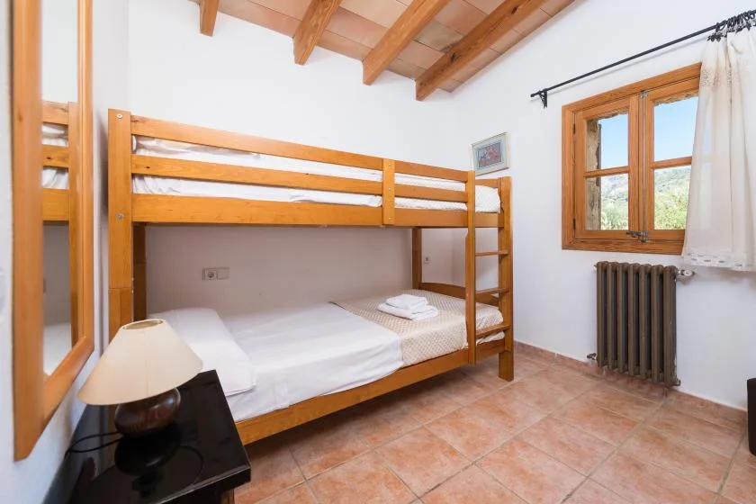 A bedroom with wooden bunk beds, white bedding, and a window.
