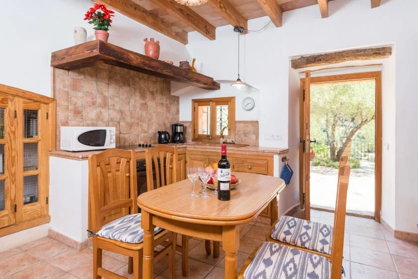 A rustic kitchen and dining area with a wooden table beside an open doorway.