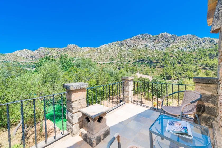 A sunny stone terrace overlooks a green valley and rocky hills.
