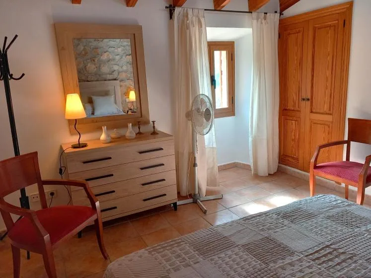 A bedroom with a bed, wooden chairs, and a dresser beside a curtained doorway.