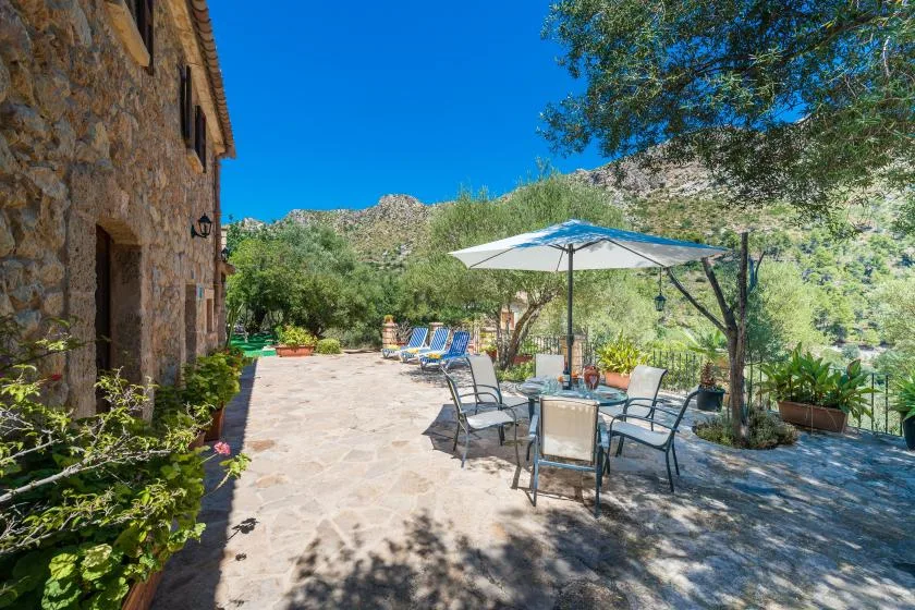 A stone patio with outdoor seating and an open umbrella overlooks a green hillside.
