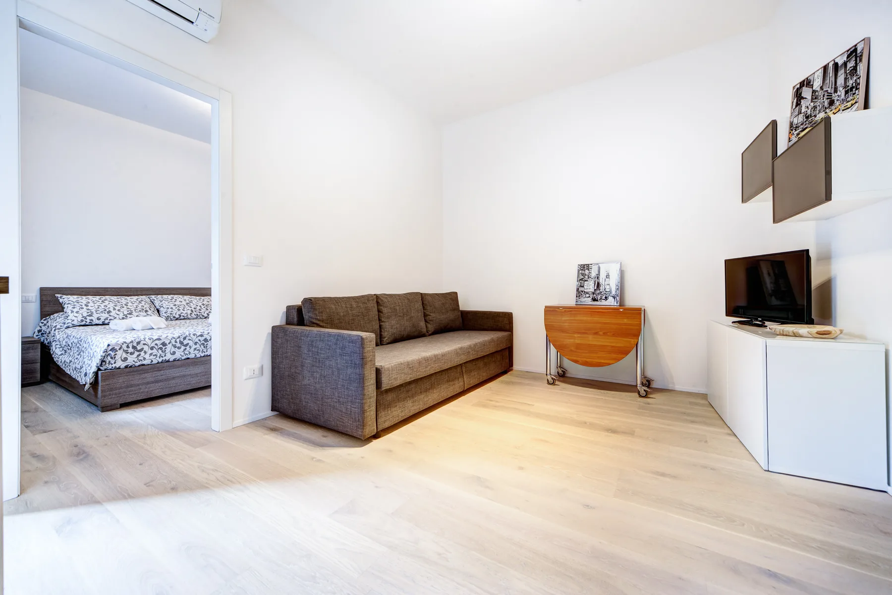 Una luminosa sala de estar con asientos, un televisor y vista abierta al dormitorio.