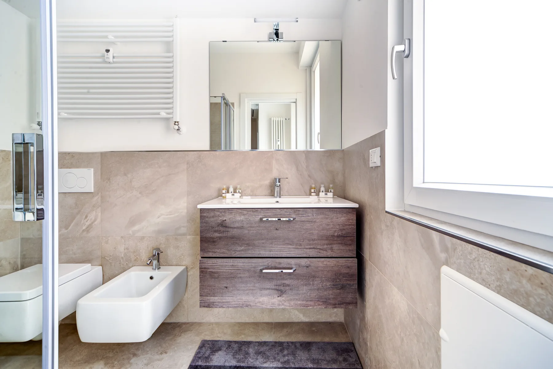 Un baño con lavabo, espejo, bidé y radiador de pared.