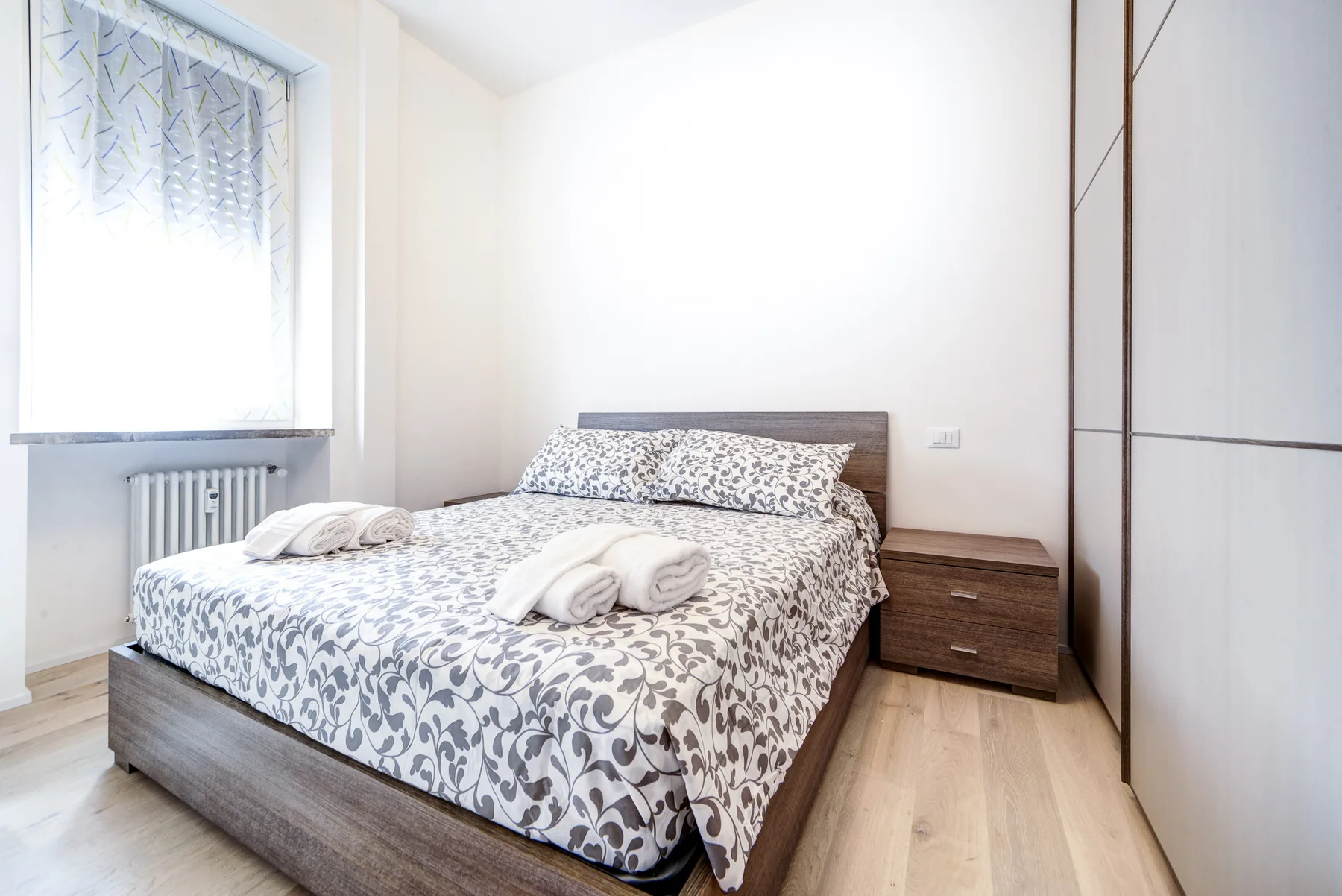 Un dormitorio con una cama estampada, una mesita de noche y una ventana.