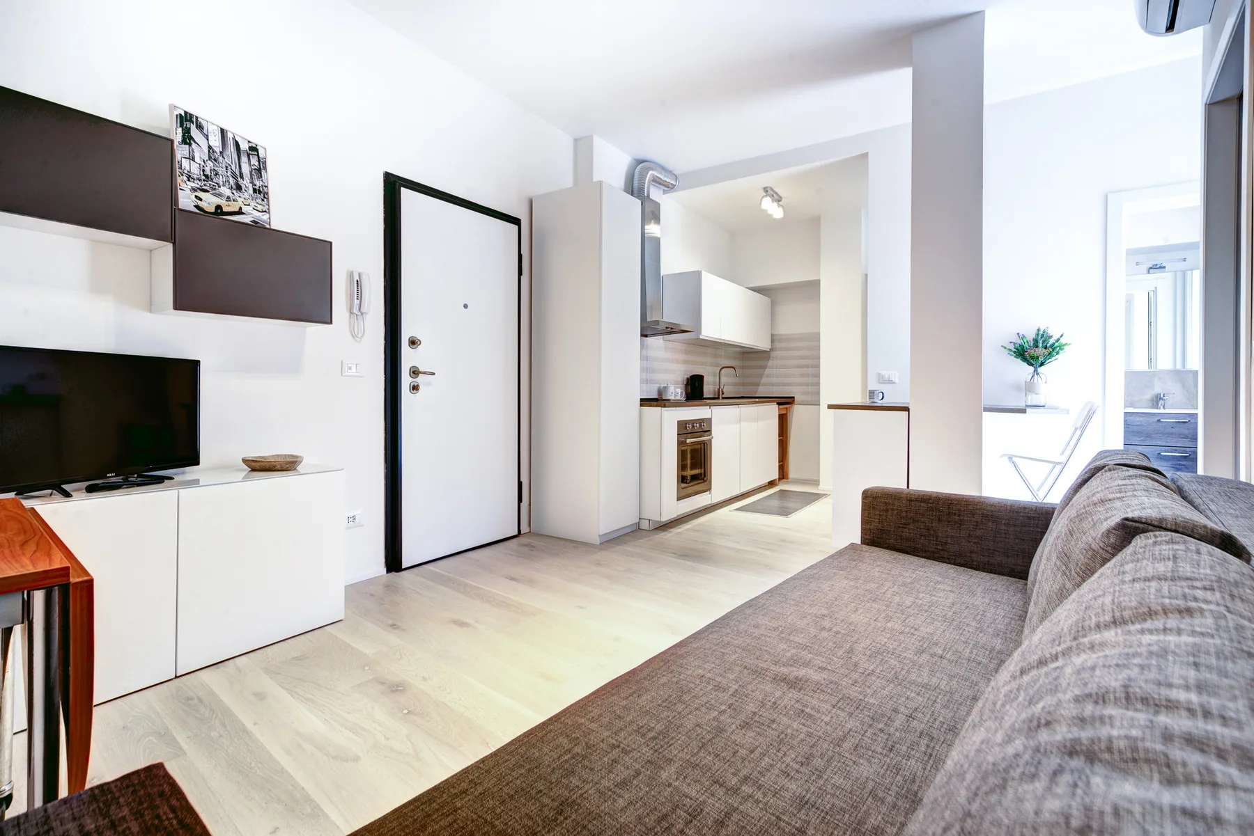 Una luminosa sala de estar con sofá, televisor y cocina compacta.