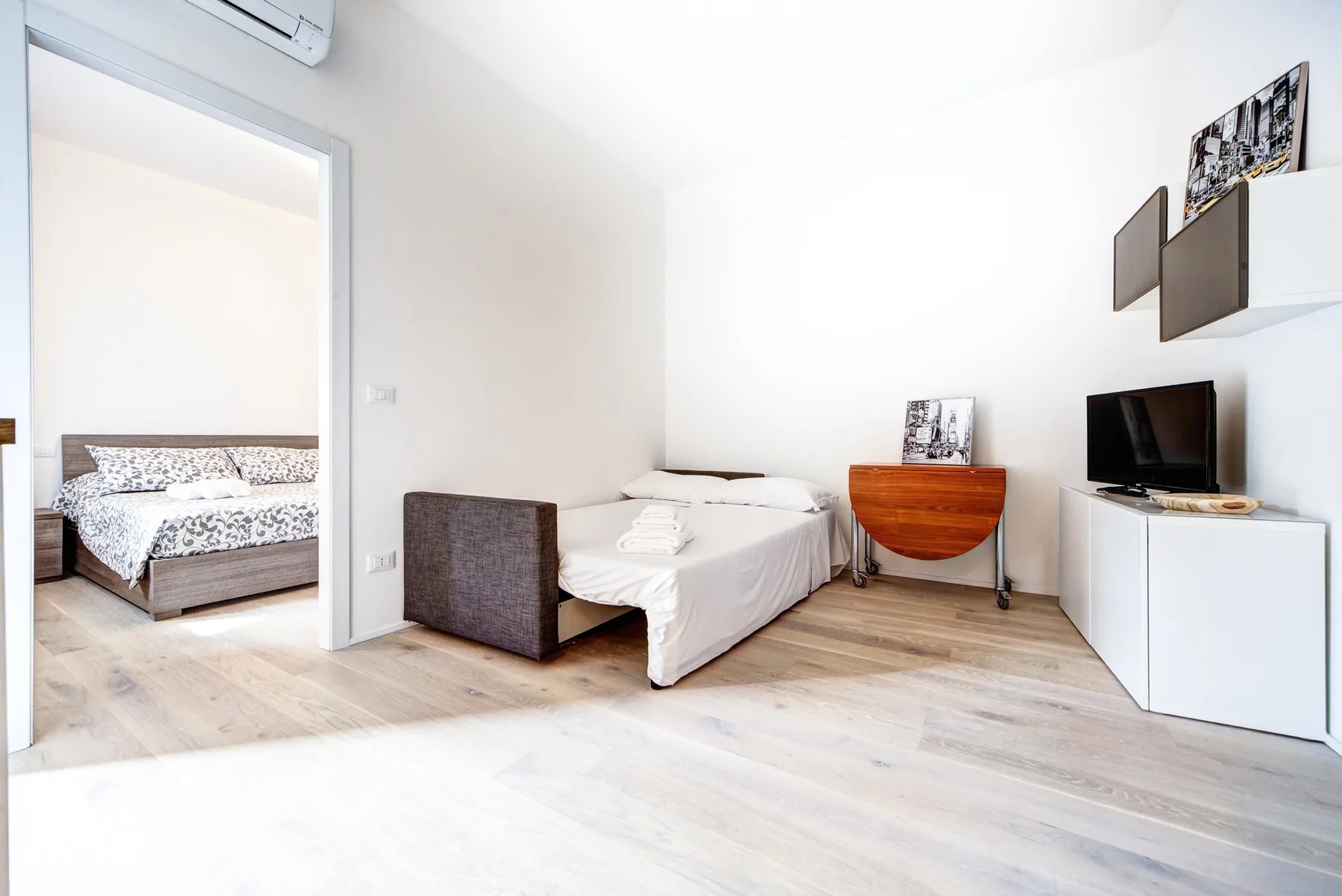 Un dormitorio luminoso con una cama, un escritorio pequeño y un televisor.